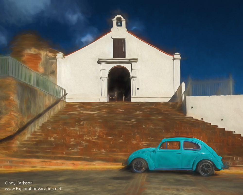 blue VW bug in front of stairs leading to a small white church